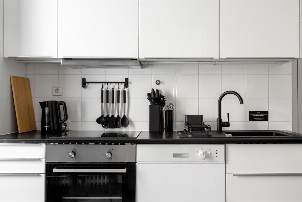 A modern kitchen with white cabinets, a black countertop, a kettle, a coffee maker, and a sink.