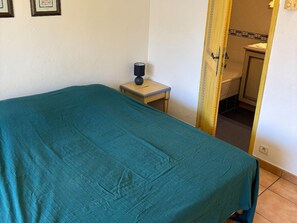 Ein Zimmer mit einem Bett, das mit türkisfarbenen Bettwäsche bezogen ist, einem kleinen Nachttisch mit Lampe und einer Tür zu einem Badezimmer.