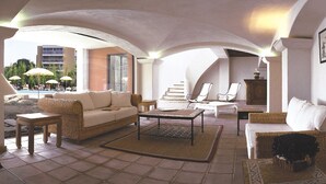 Uma sala de estar ampla com pé direito alto, vista para a área da piscina e um conjunto de estar com sofá, cadeiras e mesa de centro.