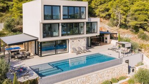 A modern two-story house with a swimming pool, outdoor seating, and a view of a forested hillside. - Breathtaking Villa Vis Five Bedroom Villa with the Pool (Vis)