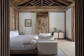 A bedroom with a large bed, a bedside table, a nightstand, a wall-mounted painting, and a stone accent wall.