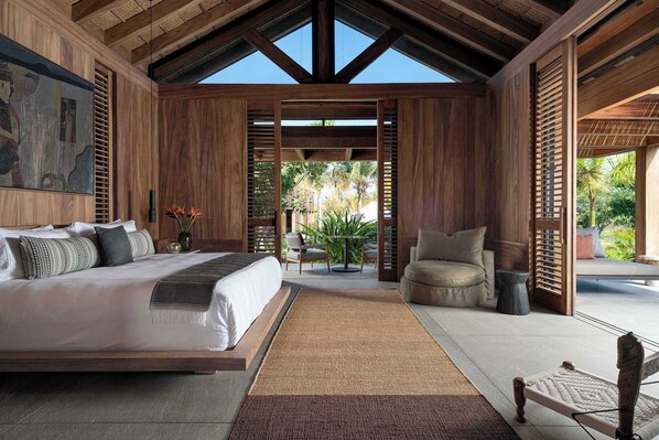A spacious bedroom with a large bed, a wooden ceiling, and a view of the outdoors.