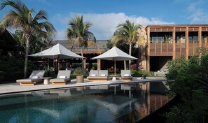 A pool area with lounge chairs and umbrellas, surrounded by tropical plants and a modern building.