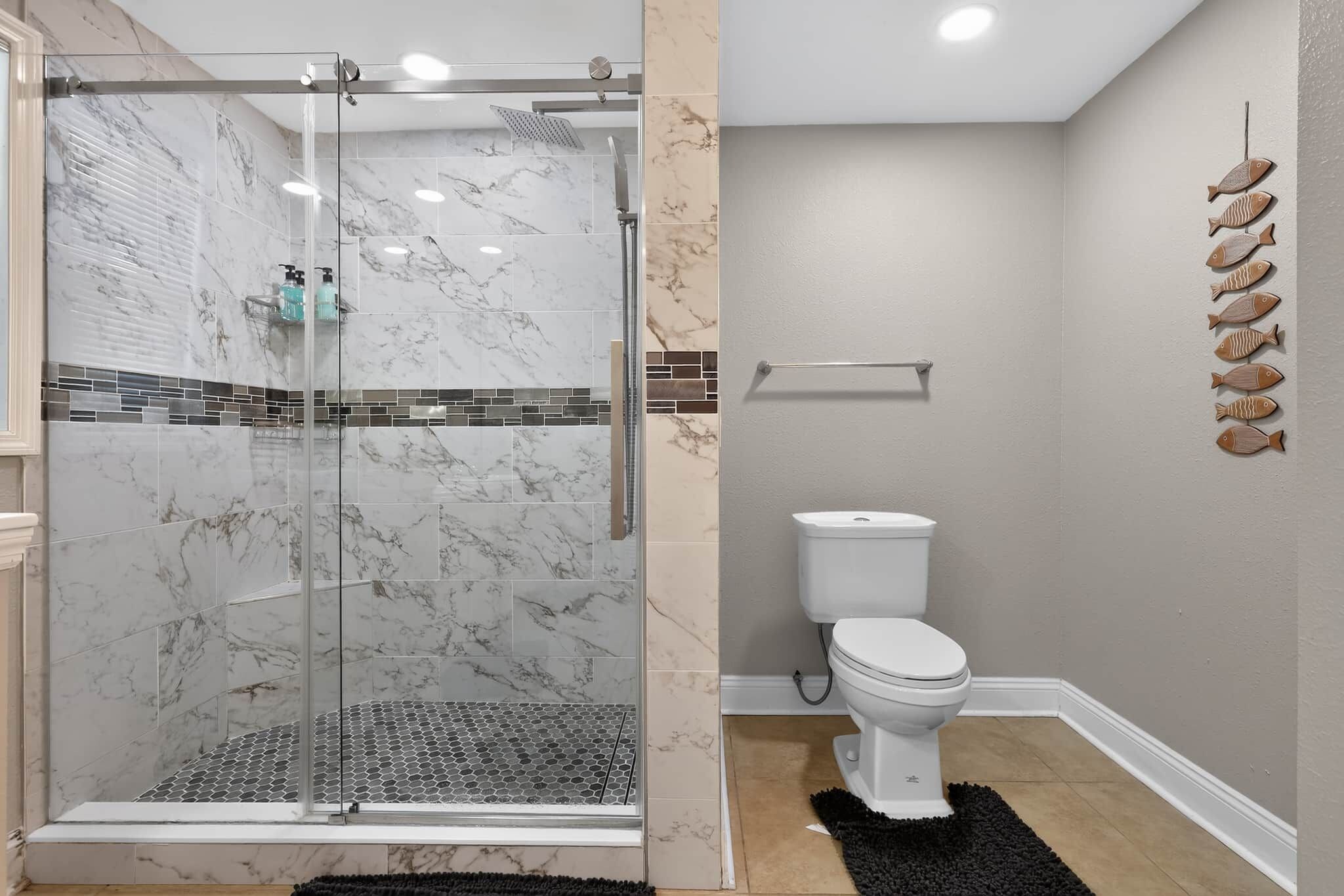 A bathroom with a glass-enclosed shower, a toilet, and a wall-mounted shelf.