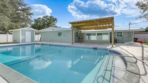 A swimming pool with a wooden pergola, a covered patio, and a small building with a door. - The Angler's Dream- Beautiful 4BR Home & HUGE Pool (Clewiston)