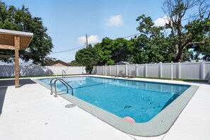Una piscina rectangular amb una escala metàl·lica, envoltada per una tanca blanca, sota un cel serè.