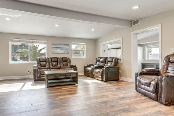 A spacious living room with leather recliners, a coffee table, and large windows.
