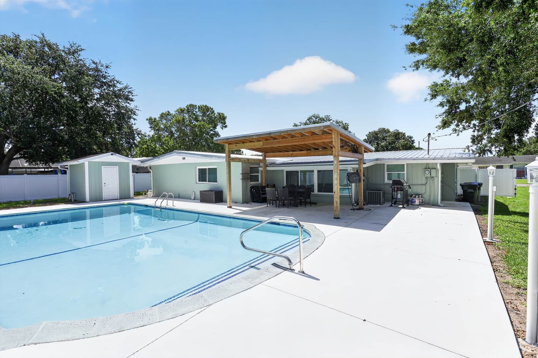 Un patio trasero con piscina, un área de patio techada y una construcción pequeña.