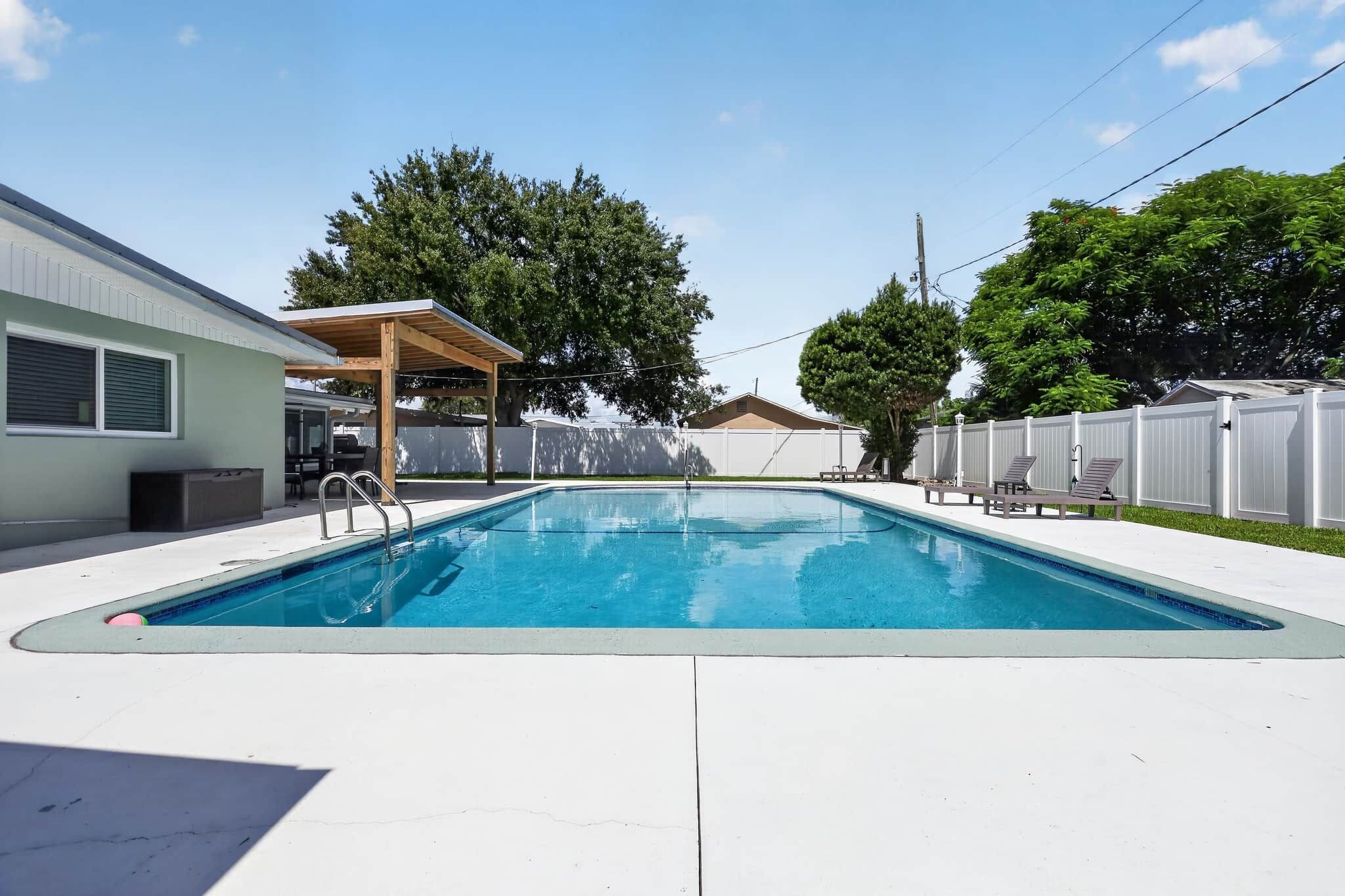 A rectangular swimming pool with a wooden deck and a covered seating area.