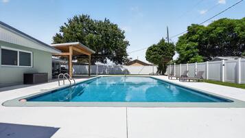A rectangular swimming pool with a wooden deck and a covered seating area.