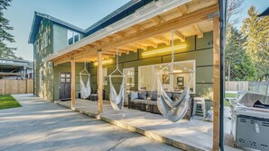 A modern house with a covered patio area featuring hanging hammocks, a barbecue grill, and a cozy seating area. - Stylish Everett Home w/ Green Belt! (Everett)