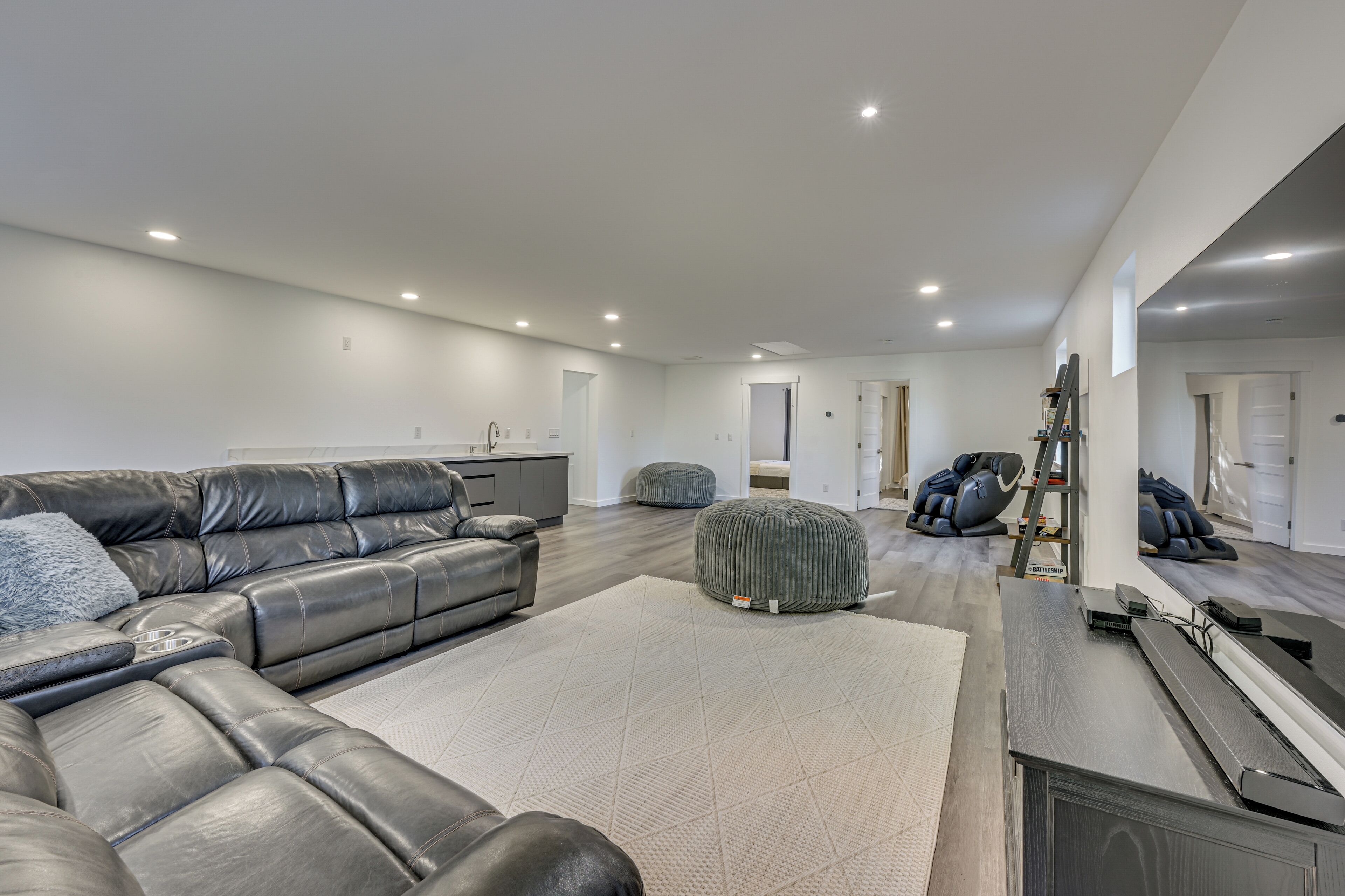 A spacious living room with a large leather sectional sofa, ottomans, and a treadmill.
