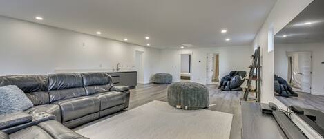 A spacious living room with a large leather sectional sofa, ottomans, and a treadmill.