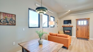 A modern living room with a wooden dining table, an orange sofa, a TV mounted on the wall, and a wooden door. - 1 Mi to Main Street: Extended Stay in Buena Vista! (Buena Vista)