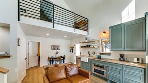 Un vaste espace de vie comprenant un canapé en cuir marron, une table à manger et une cuisine dotée de meubles turquoise et d’appareils électroménagers modernes.