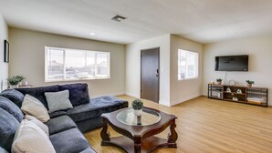 A spacious living room with a dark grey sectional sofa, a round wooden coffee table, and a flat-screen TV mounted on the wall. - Beautiful 4-bedroom apartment with AC in peaceful San Diego (San Diego)