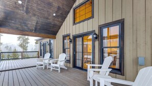Una terraza cubierta con sillones Adirondack blancos y una mesa, paredes de madera y ventanas amplias.