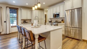 Una cocina amplia con armarios blancos, un refrigerador de acero inoxidable grande y una isla central con taburetes de bar.