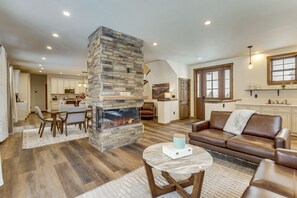 A spacious living area with a stone fireplace, leather sofa, and a dining area with wooden furniture. - Ride-In/Ride-Out Grand Lake Hub Near Lakes & RMNP (Grand Lake)