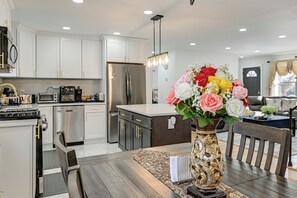 Une cuisine moderne avec des meubles blancs, des appareils en acier inoxydable et un coin repas comprenant une table et des chaises en bois.