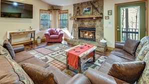 A cozy living room with a stone fireplace, leather sofas, a wooden coffee table, and a television mounted on the wall. - Hot Tub & Streamside Bliss! Topton Mtn Haven (Topton)