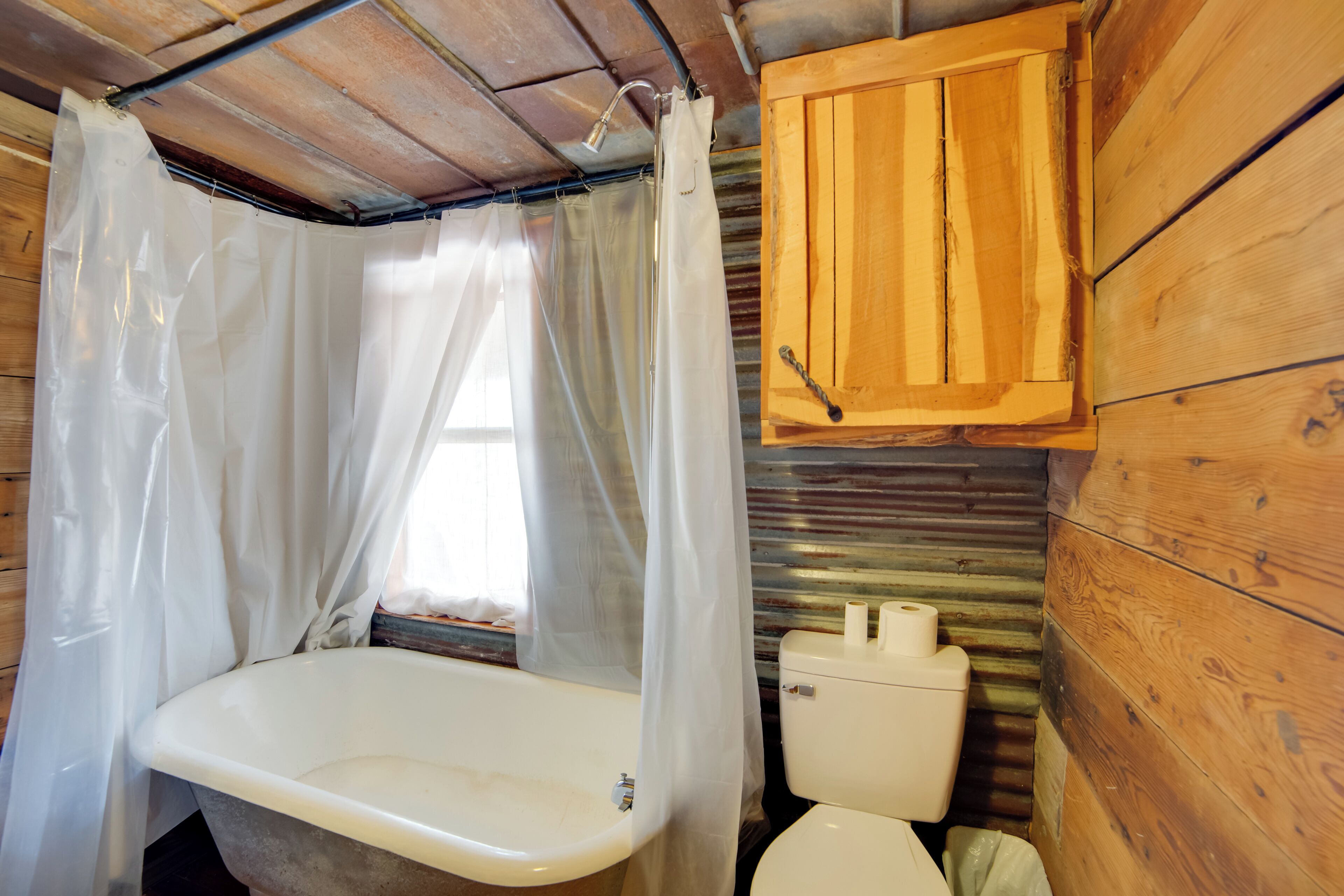 Ein rustikales Badezimmer im Holzblockhausstil, mit einer Badewanne, Toilette und Holzschränken.