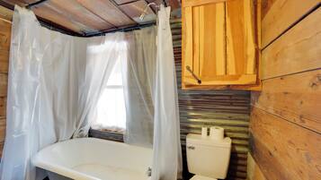 Ein rustikales Badezimmer im Holzblockhausstil, mit einer Badewanne, Toilette und Holzschränken.