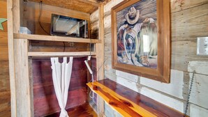 Interior rústico de una cabaña de madera con un televisor montado, un cuadro enmarcado de un vaquero y una estantería de madera.
