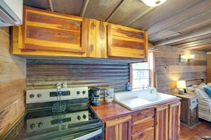 A rustic kitchen with wooden cabinets, a stove, a coffee maker, and a sink. - Couple’s Getaway w/ Ranch Views - Near Lavon Lake! (Blue Ridge)