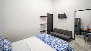 A small, modern room with a bed, a sofa, a TV mounted on the wall, a refrigerator, and a door. - Downtown Apartment by The Beach #5 (Sámara)