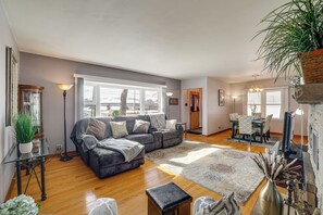 A spacious living room with a grey sofa, a coffee table, and a fireplace. There is a dining area with a table and chairs. - Spacious & Peaceful Suburban Home in Lansing! (Lansing)