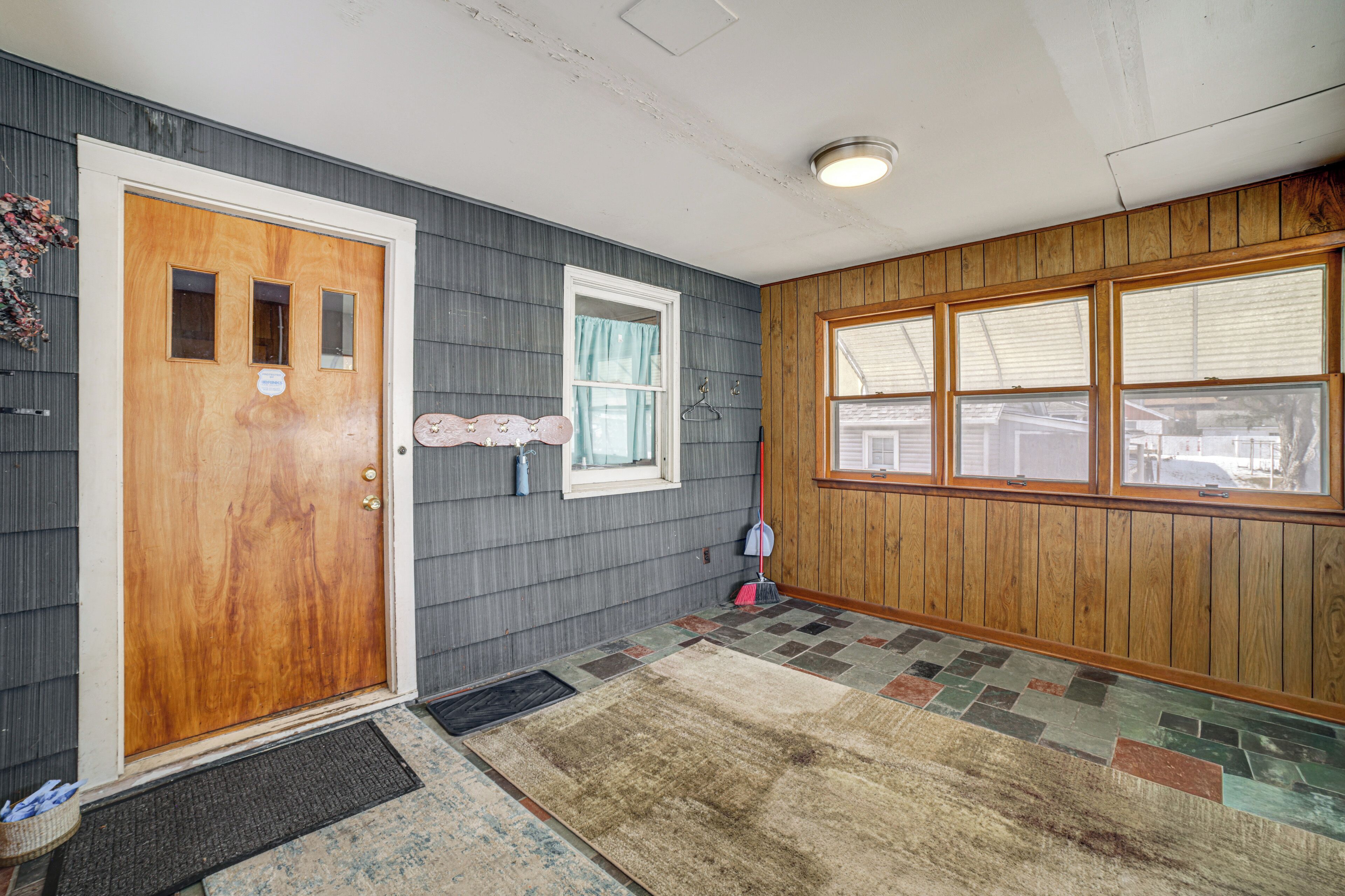 A hallway with a wooden door, a window with a curtain, and a patterned rug.