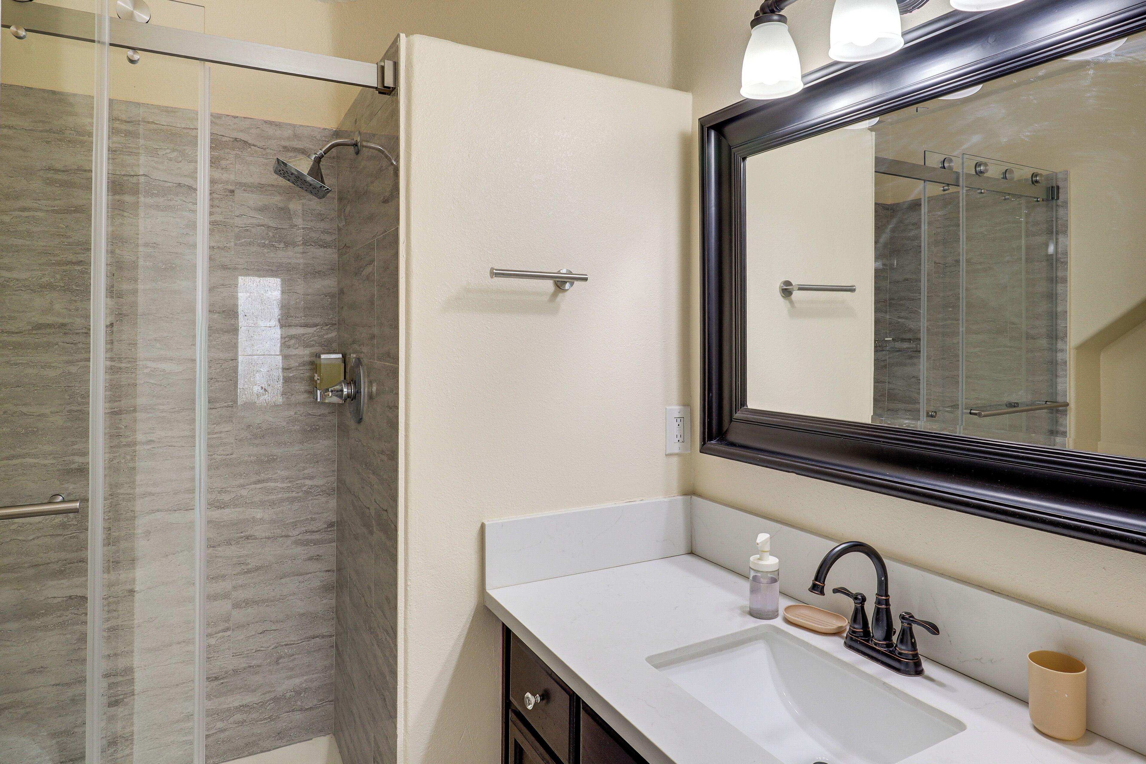 Une salle de bain moderne avec une douche à l’italienne en verre, un lavabo blanc avec un robinet noir et un grand miroir au-dessus du lavabo.
