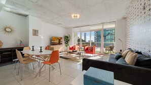 A modern living room with a dining area, large windows, and a city view. - Midtown Rouge- Condo with City Views, Pool & Gym (Miami)