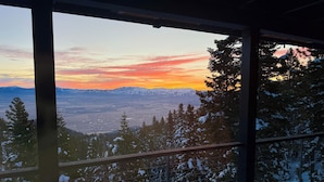 Blick aus einem Fenster auf verschneite Bäume und Berge bei Sonnenuntergang.