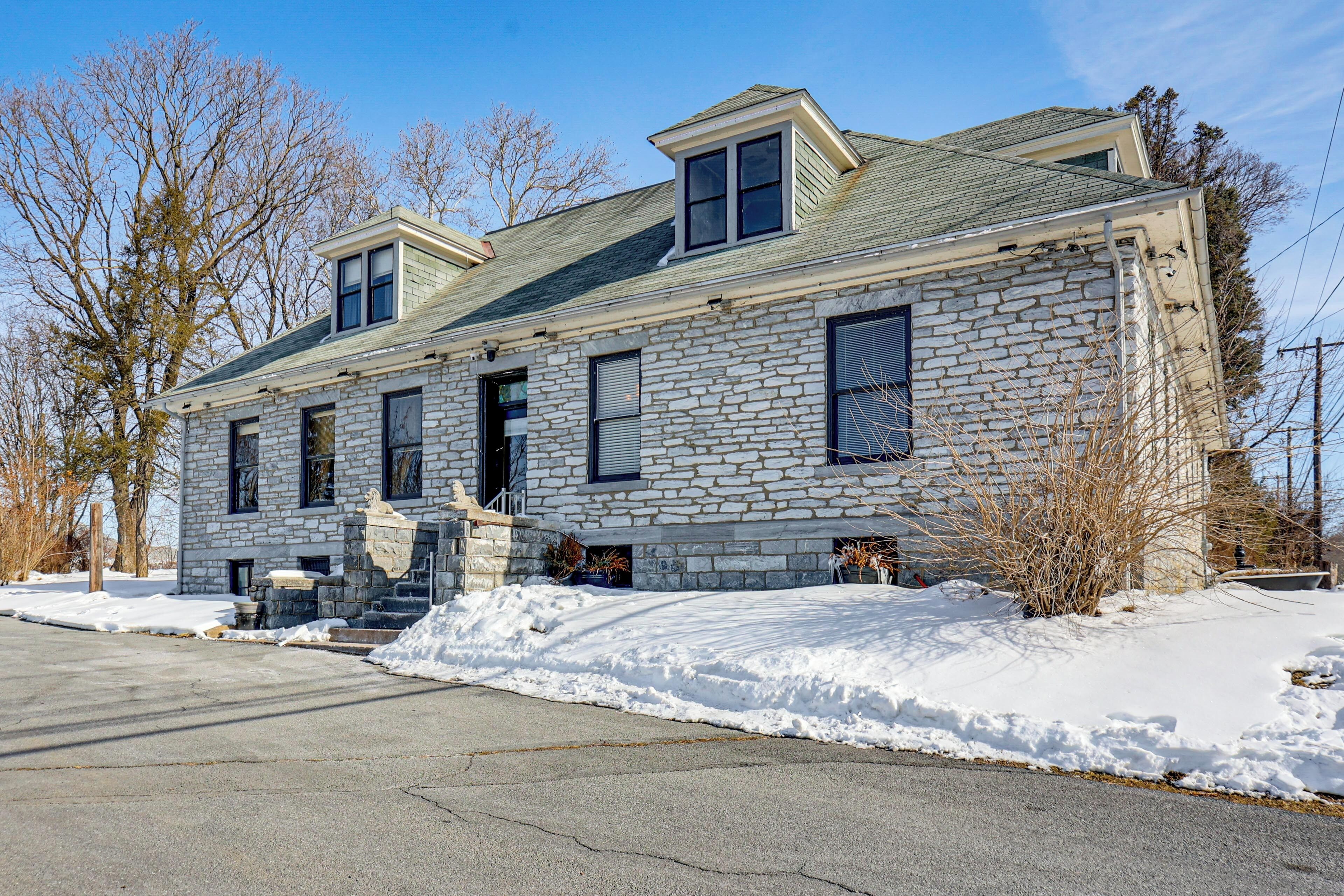 A stone house with a gabled roof, a front porch, and a small front yard with snow.