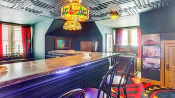 Uma área de bar com um balcão comprido, várias cadeiras, um lustre e um tapete colorido.