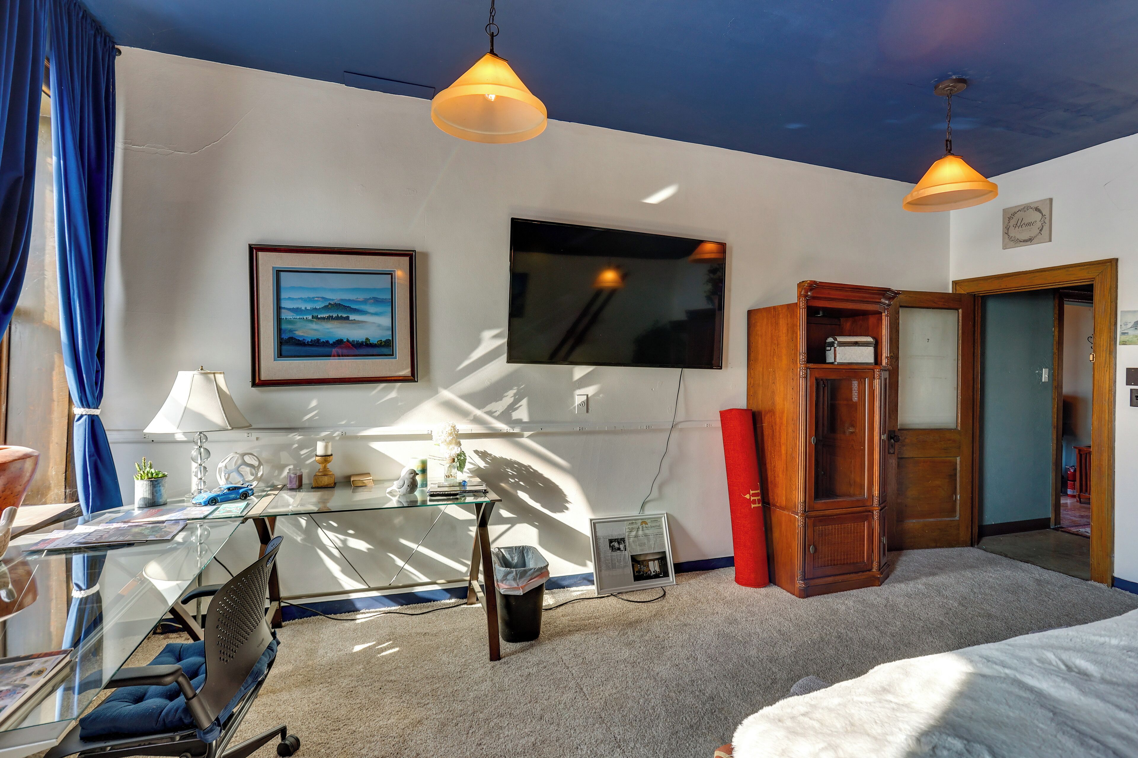 A hotel room with a glass desk, a bed, a TV, and a wooden wardrobe.