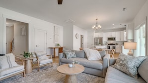 A modern living room with a grey sofa, wooden coffee table, and a kitchen in the background. - 4 Mi to Surf City Beaches! Family Coastal Retreat (Hampstead)