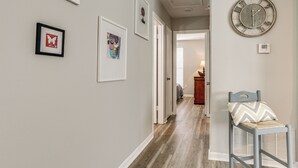 A hallway with framed artwork on the walls, a clock, and a chair with a cushion. - 1 Mi to Tiger Stadium: Sleek University South Gem! (Baton Rouge)