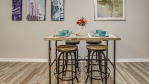 A dining area with a table set for two, two stools, and three framed artworks on the wall. - 1 Mi to Tiger Stadium: Sleek University South Gem! (Baton Rouge)