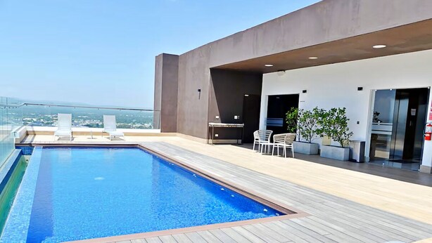 Ein Pool auf dem Dach mit Holzterrasse, Liegestühlen und einem modernen Gebäude mit Glasfassade.