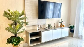 Ein modernes Wohnzimmer mit einem an der Wand befestigten Flachbildfernseher, einem weißen Konsolentisch mit Dekoration und einer großen Küsterpflanze.