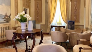 A room with a large window, a painting on the wall, and a table with a vase of flowers.