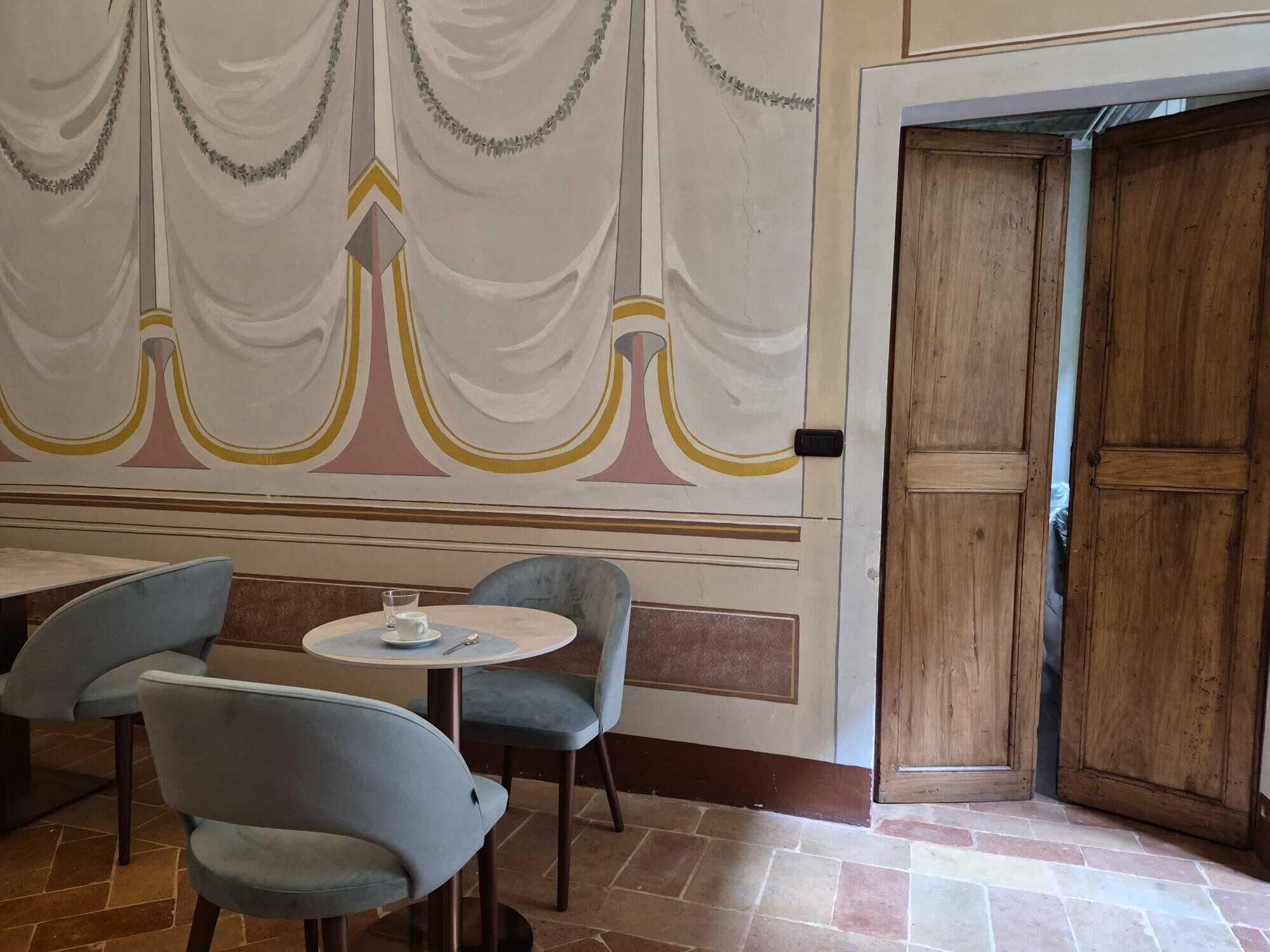 A room with a table and two chairs, a wooden door, and a wall with a decorative design.