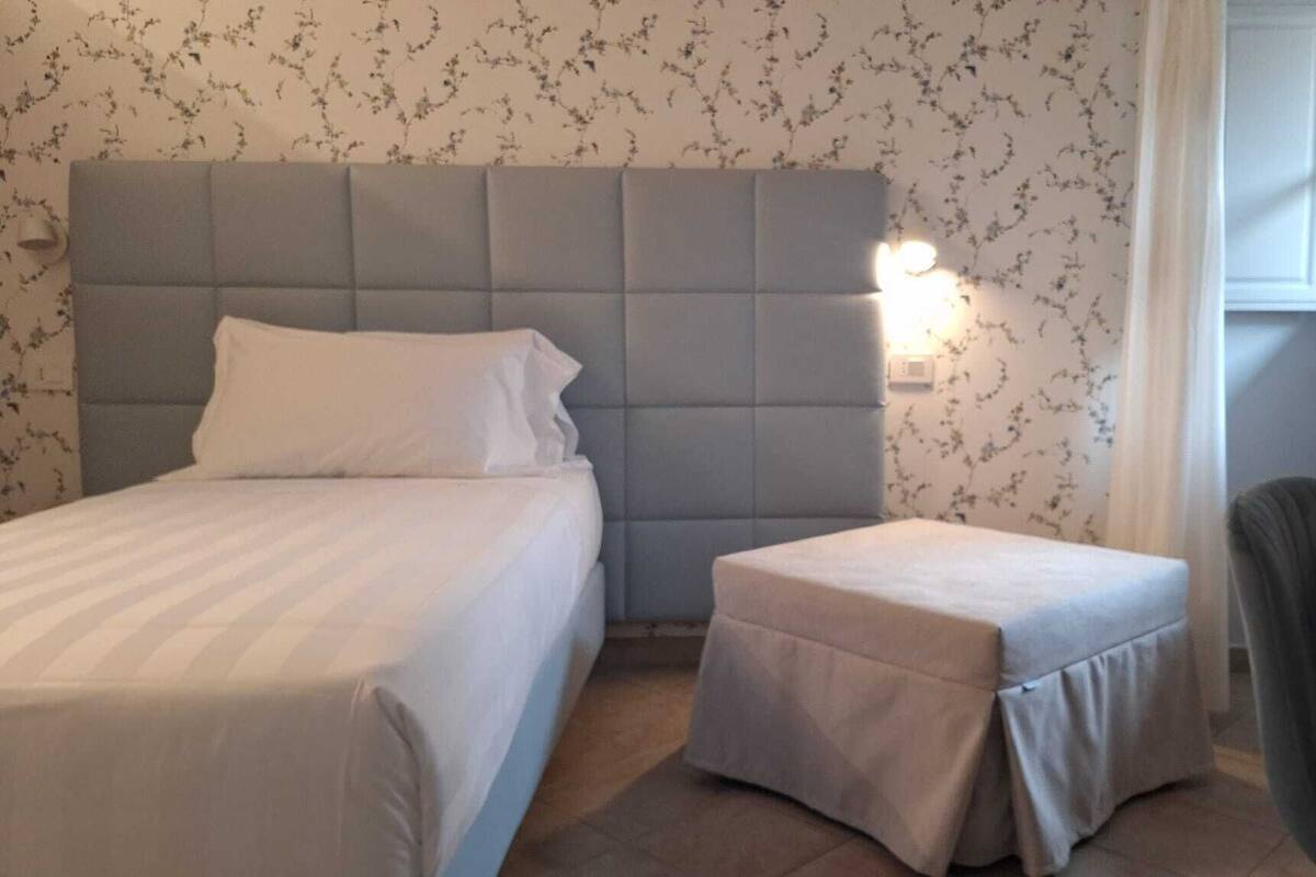 Un dormitorio con una cama, una mesita de noche, una silla y una lámpara en la pared.