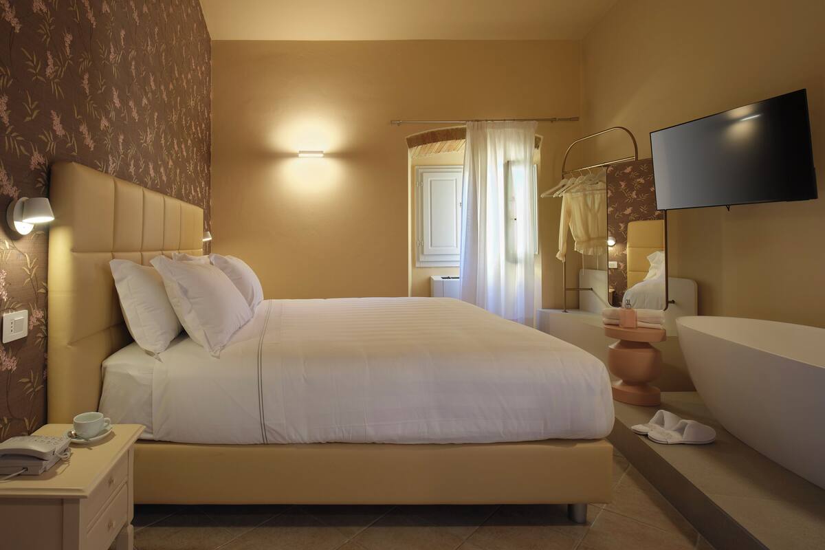 Un dormitorio de hotel con cama, mesita de noche, televisor y bañera.