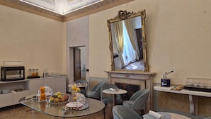 A hotel room with a dining area, a fireplace, a mirror, and a breakfast bar with beverages.