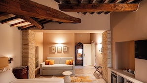 A bedroom with a bed, a sofa, a small table, a TV, and a fireplace.