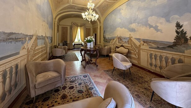 A luxurious room with a grand chandelier, elegant furniture, and a scenic mural on the walls.